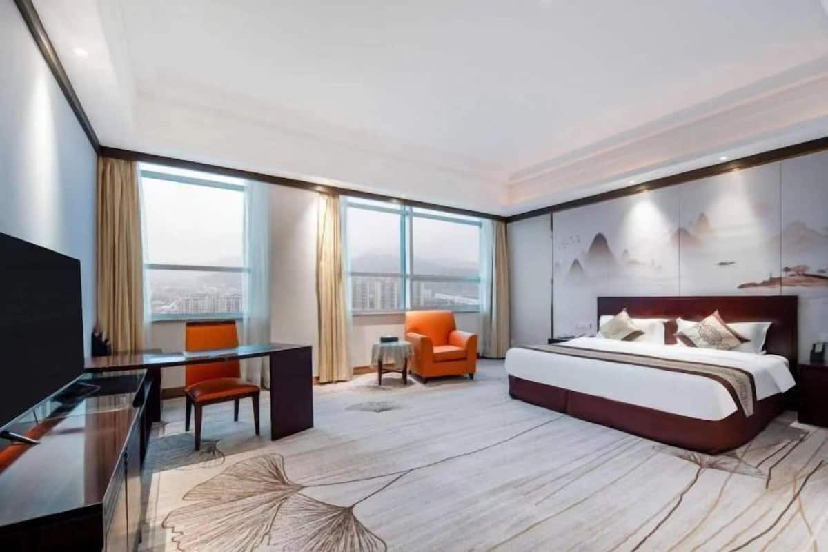 A modern hotel room with a large bed, a desk, an orange chair, and a city view.