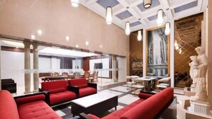 A spacious lobby with red seating, a large mirror, and a statue. - Hailiang Business Hotel (Zhuji)