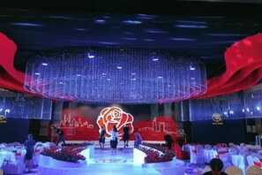 A stage with a large illuminated rose and a city skyline backdrop, surrounded by tables with white tablecloths. - Hailiang Business Hotel (Zhuji)