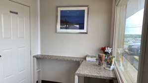 A hallway with a white door marked "Employees Only," a framed picture on the wall, a small table with magazines and a vase of flowers, and a window with a view of a parking lot. - Regency Inn (Rolla)