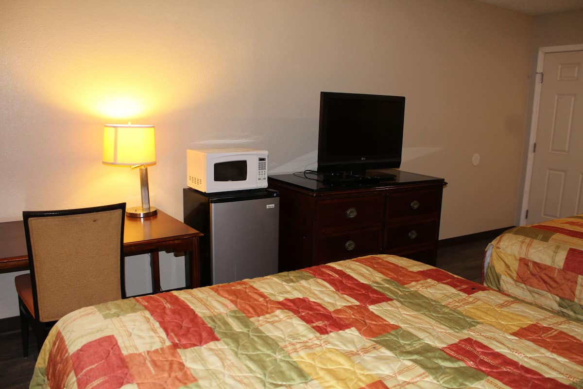 A hotel room with a bed, a television on a dresser, a microwave, a refrigerator, and a lamp.