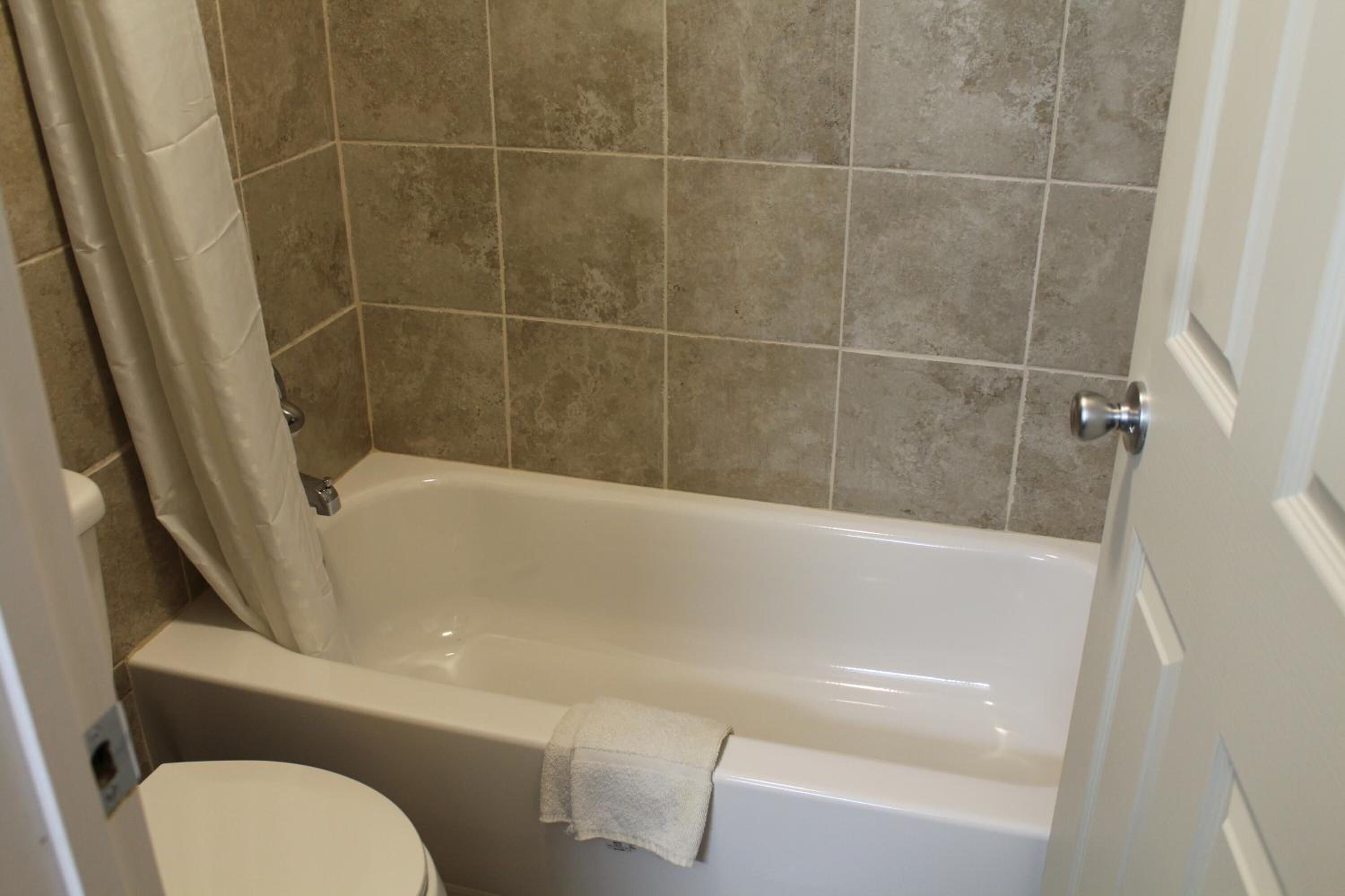A bathroom with a bathtub, toilet, and beige tiled walls.