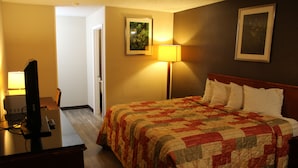 A hotel room with a bed, a desk with a computer, a lamp, and a painting on the wall. - Regency Inn (Rolla)
