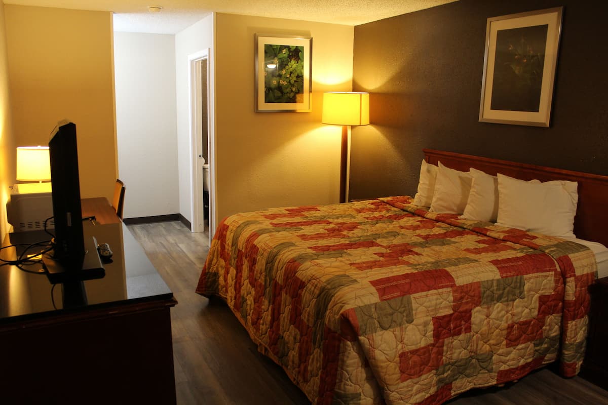 A hotel room with a bed, a desk with a computer, a lamp, and a painting on the wall.