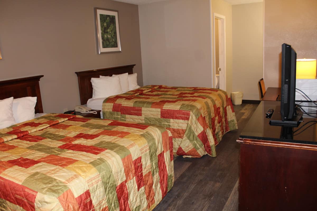 A hotel room with two beds, a desk with a television, and a door leading to another room.