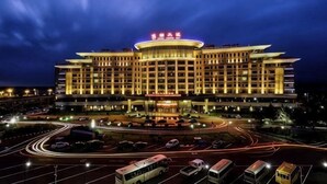 Un grand hôtel à plusieurs étages, doté d’un élément central circulaire bien visible, de nombreux parkings et d’une façade bien éclairée.