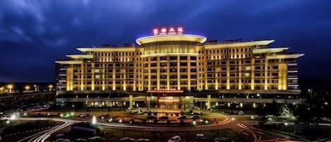 A large, multi-story hotel with a prominent circular central feature, multiple parking lots, and a well-lit facade.