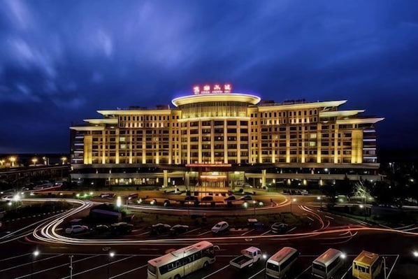 A large, multi-story hotel with a prominent circular central feature, multiple parking lots, and a well-lit facade.