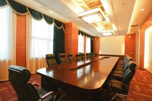 A conference room with a long table and multiple chairs, large windows with curtains, and a carpeted floor.