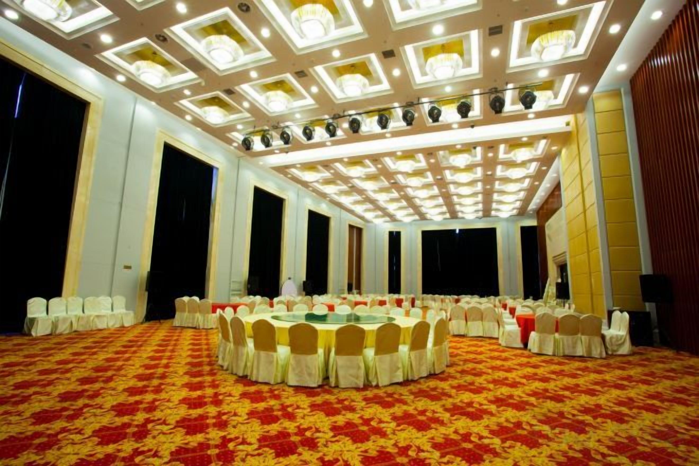 A large conference room with a round table surrounded by chairs, a patterned carpet, and a high ceiling with recessed lighting.