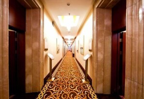 A hotel hallway with a patterned carpet, doors on either side, and a light fixture on the ceiling. - Hot Spring Leisure City International Hotel (Wudalianchi)