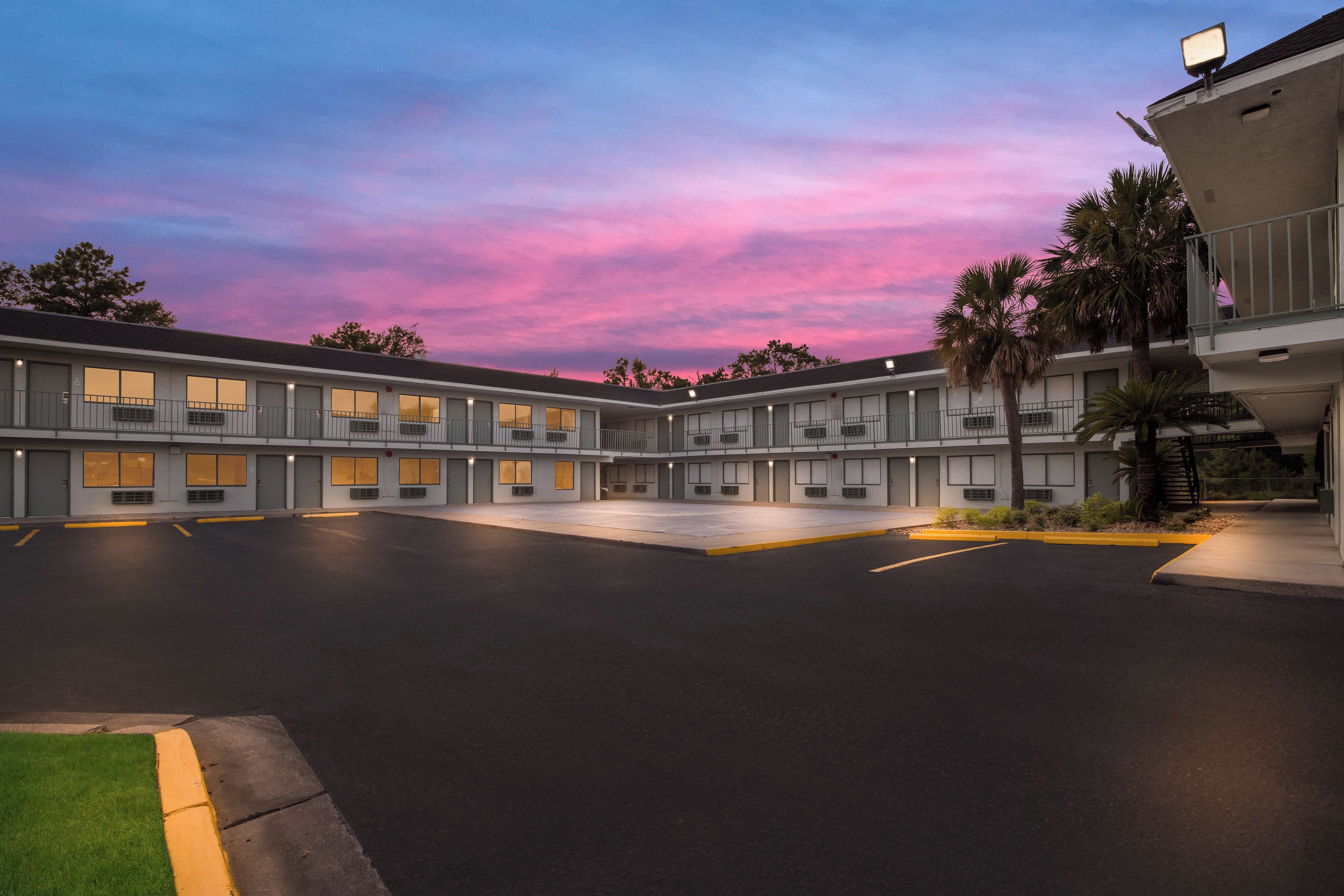 A motel with multiple rooms, a parking lot, and a view of the sky.
