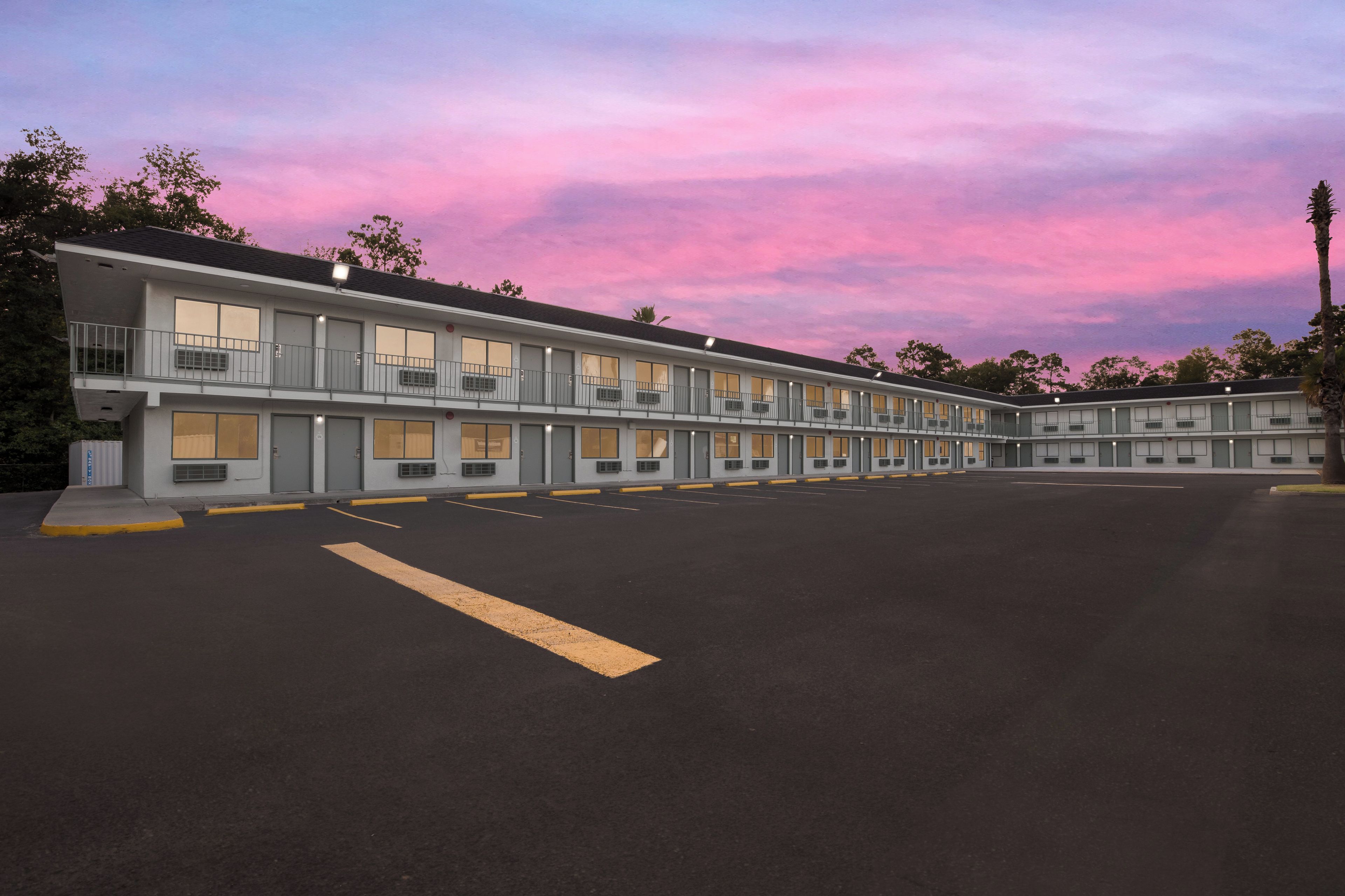 Ein Motel mit mehreren Zimmern, einem Parkplatz und wolkenlosem Himmel.
