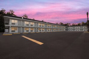 A motel with multiple rooms, a parking lot, and a clear sky. - HomeTowne Studios by Red Roof Orange, TX (Orange)