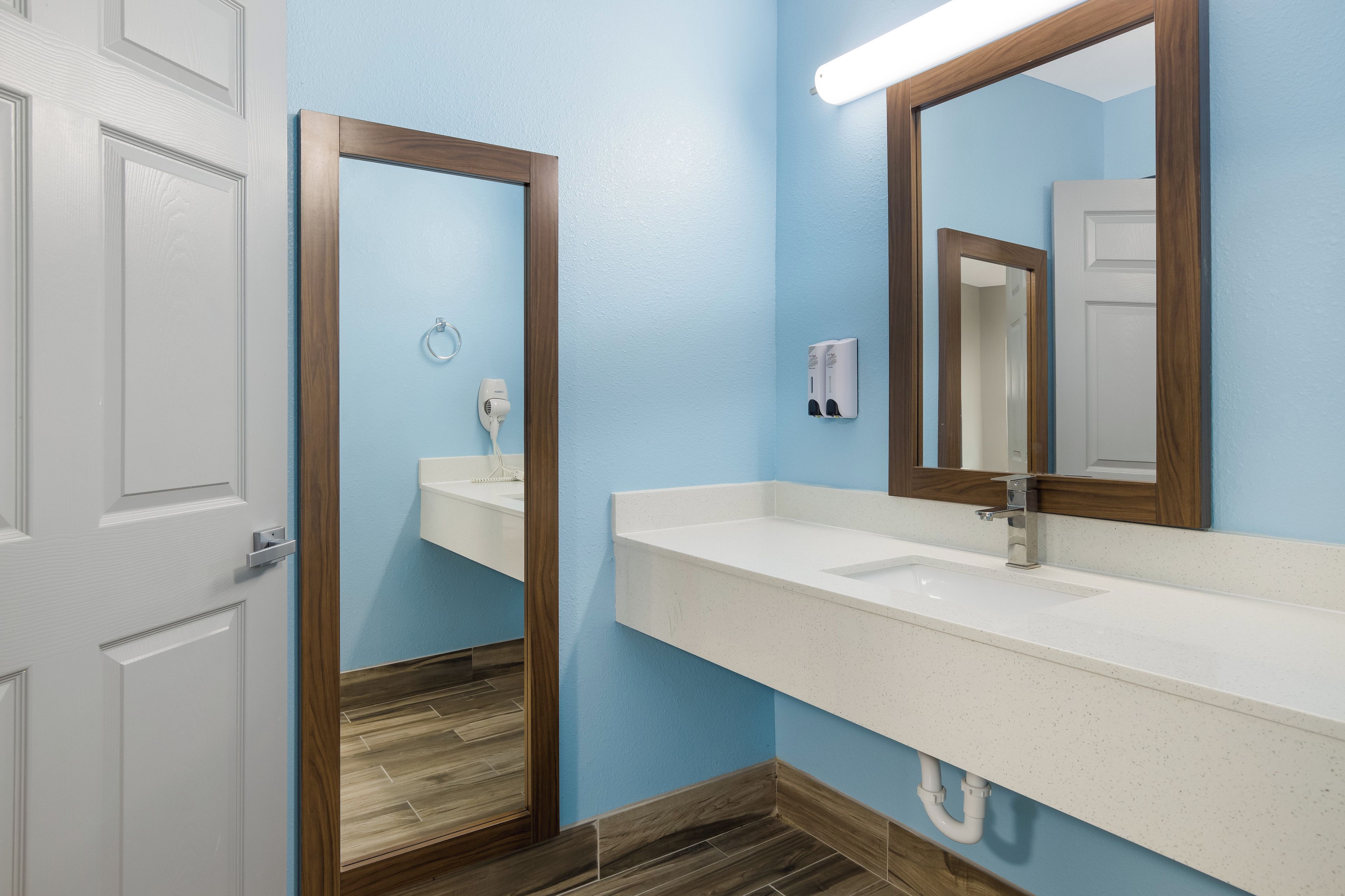 A bathroom with a white sink, a mirror, a hairdryer, and a soap dispenser.