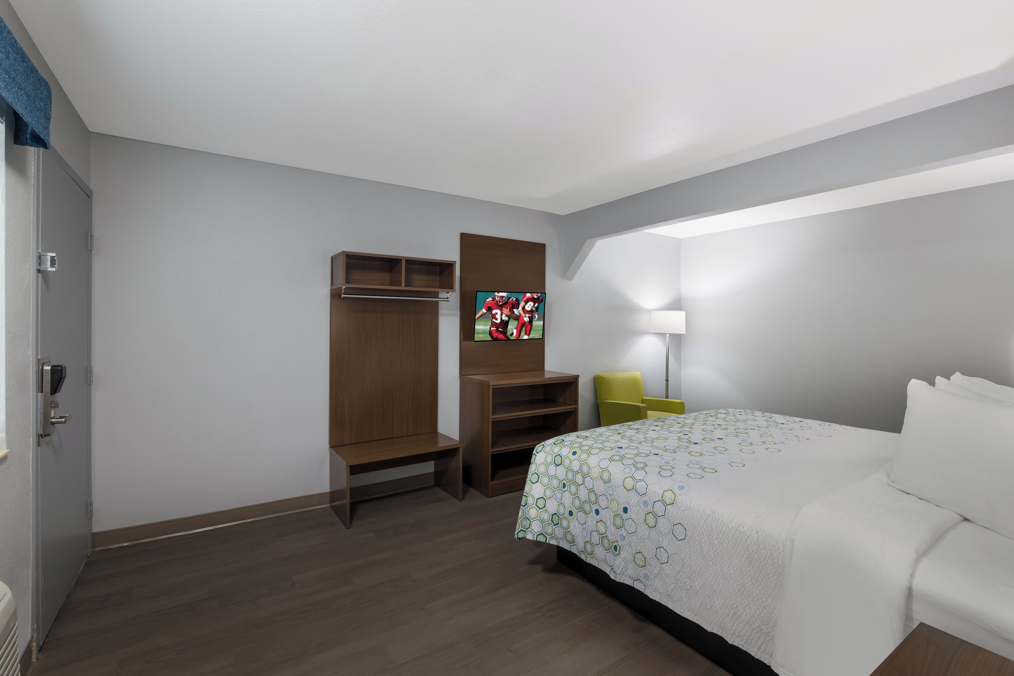 A hotel room with a bed, a desk, a chair, a TV, and a wardrobe.