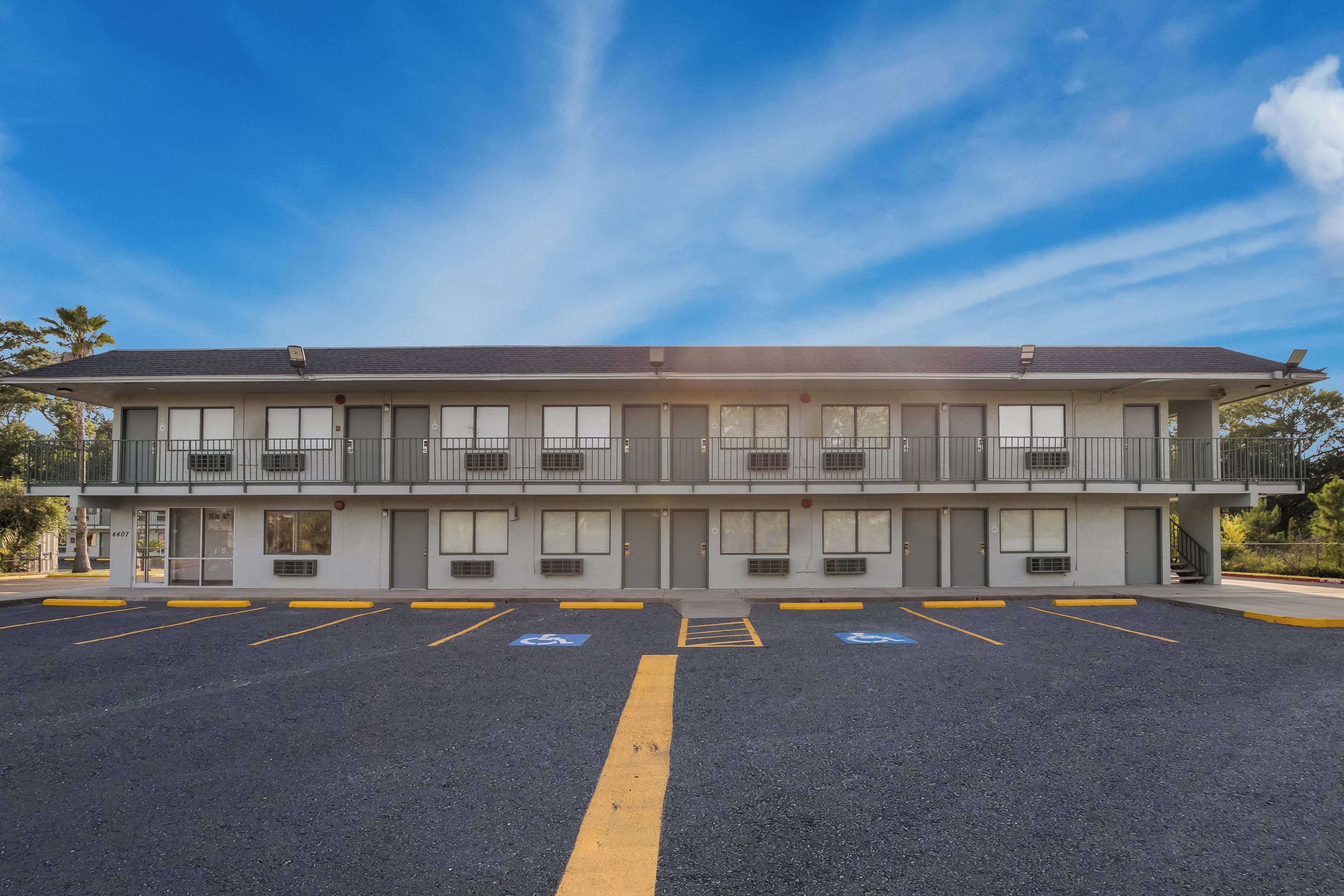 En toetages motel med parkeringsplads, tydeligt markerede handicap parkeringspladser og en klar himmel.
