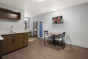 A modern kitchen with wooden cabinets, a sink, and a dining area with a table and chairs. - HomeTowne Studios by Red Roof Orange, TX (Orange)