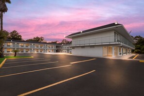 A motel with a large parking lot and a building with multiple windows and balconies. - HomeTowne Studios by Red Roof Orange, TX (Orange)