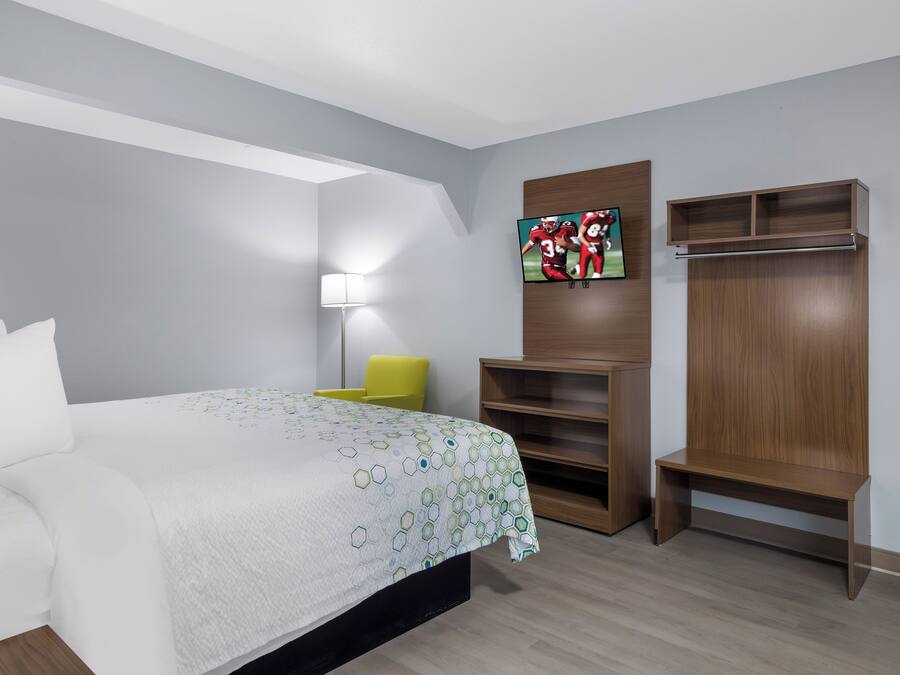 Une chambre d’hôtel avec un lit, un téléviseur fixé au mur, une chaise et une armoire en bois.