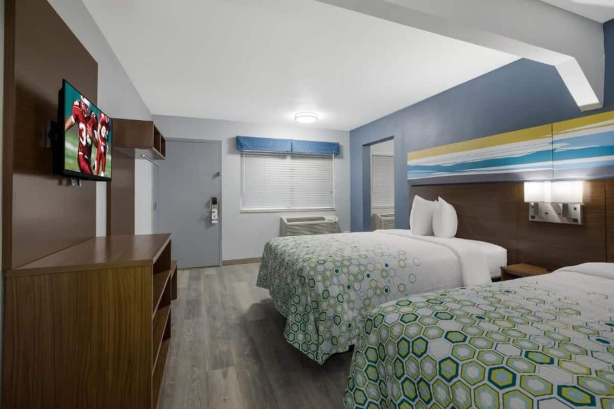 Ett hotellrum med två sängar, en TV, ett skrivbord och ett fönster med persienner.