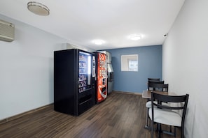 A compact room with a dining table and chairs, two vending machines, and a window. - HomeTowne Studios by Red Roof Orange, TX (Orange)