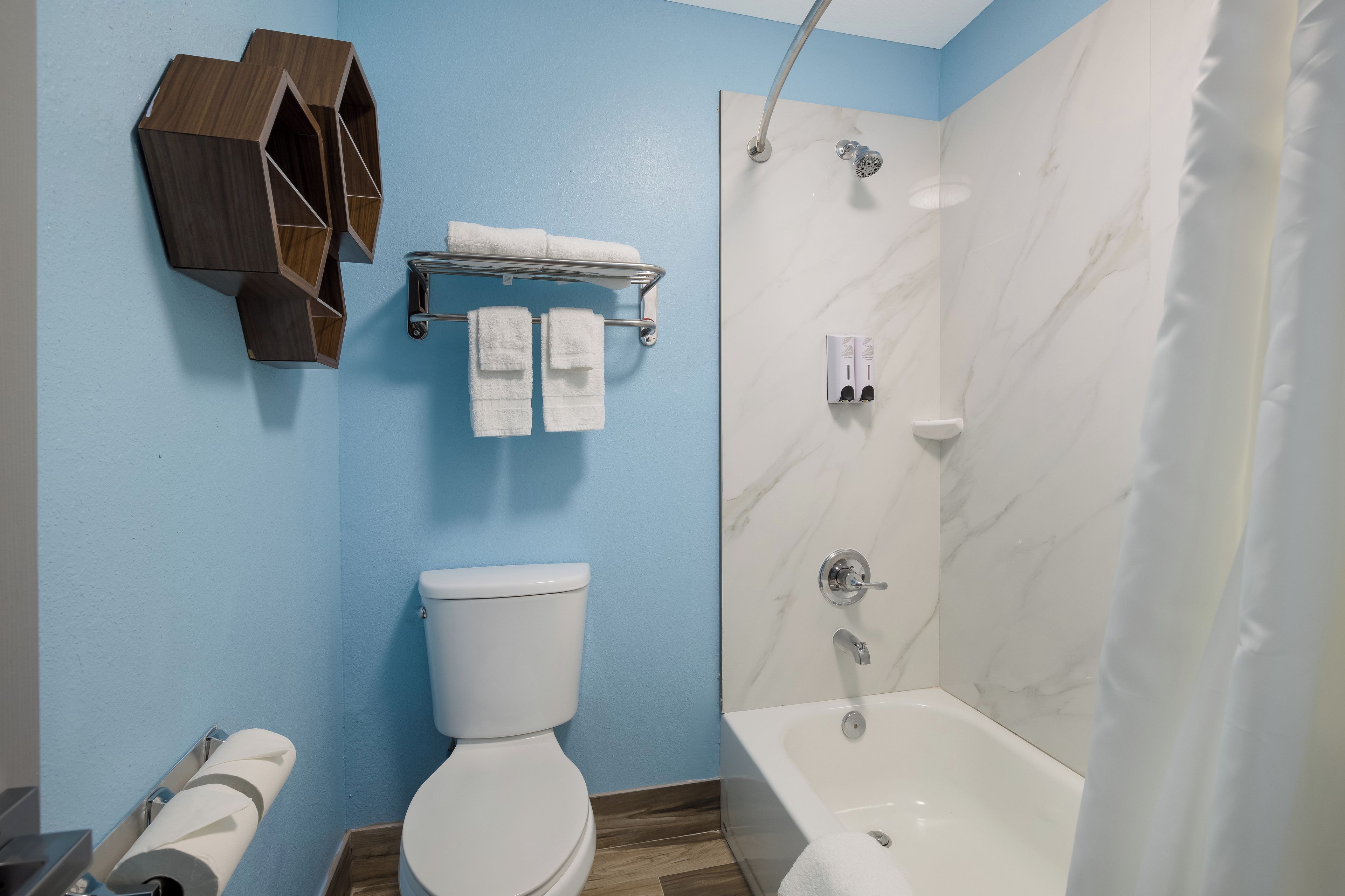 A bathroom with a toilet, a shower, a towel rack, and a toilet paper holder.