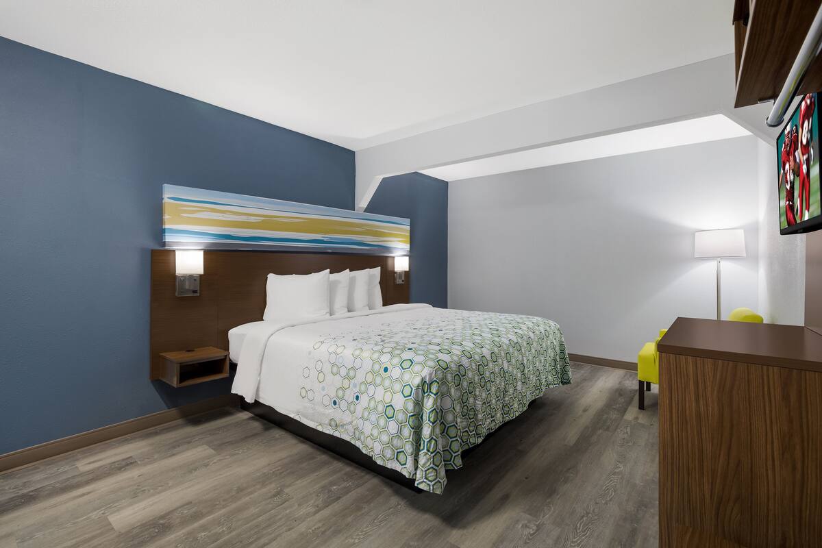 Ett modernt hotellrum med en säng, ett sängbord, ett skrivbord och en stol.