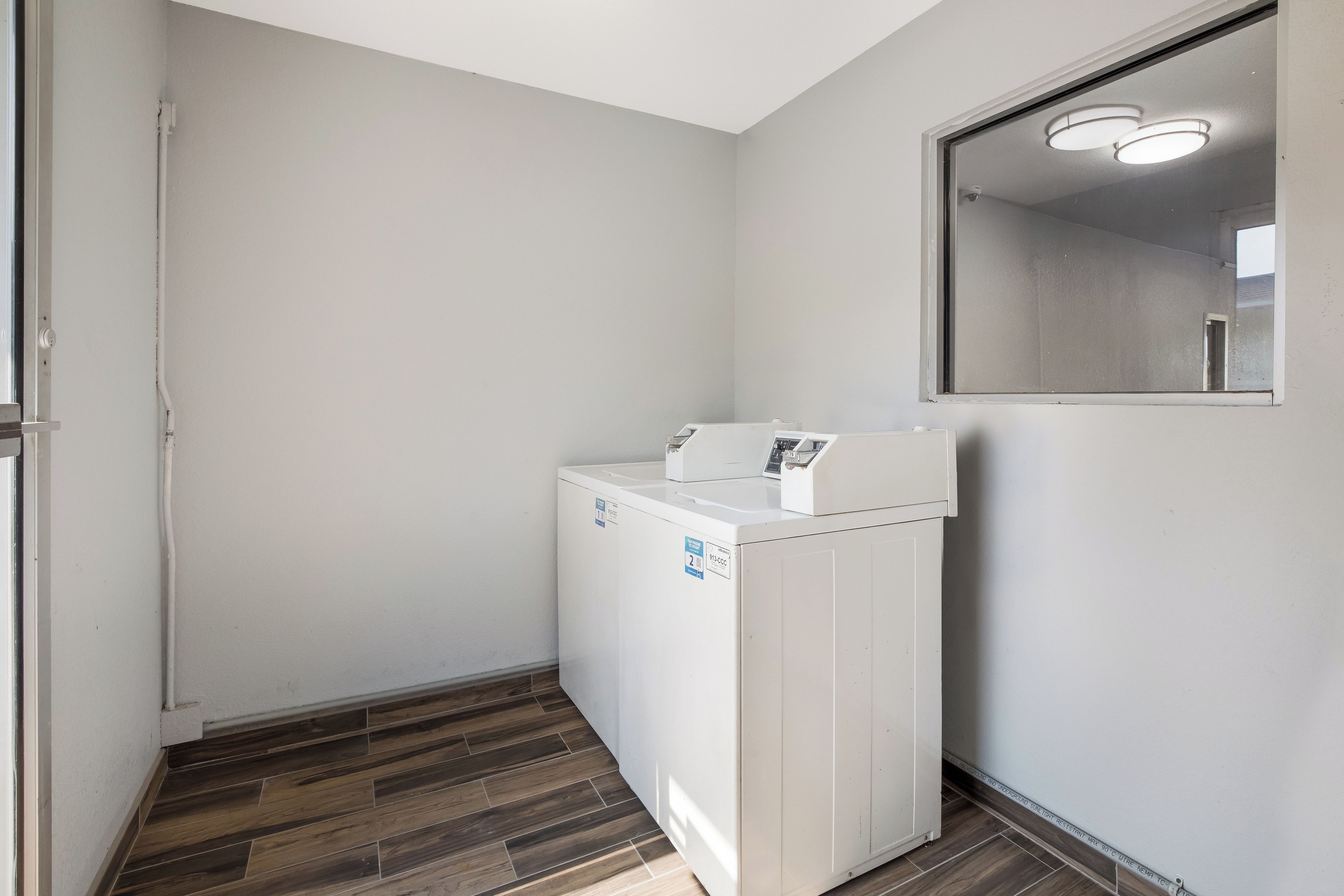 A laundry room with a washing machine, a door, and a wooden floor.
