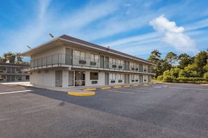 A multi-story motel with a flat roof, multiple balconies, and a parking lot with yellow curbs. - HomeTowne Studios by Red Roof Orange, TX (Orange)