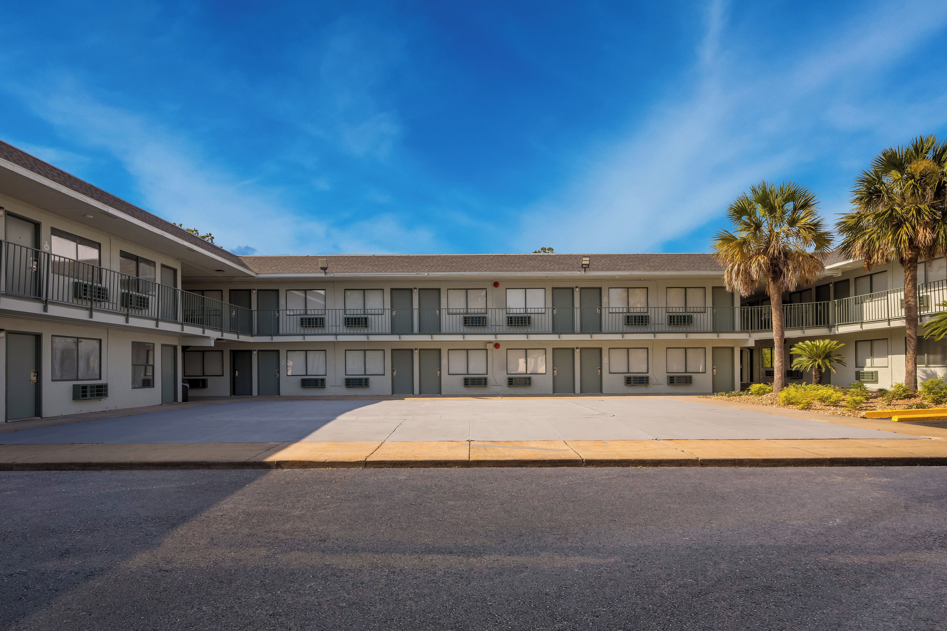 Een motel met meerdere verdiepingen, een centrale binnenplaats, balkons en palmbomen.