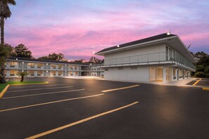 A motel with a large parking lot and a building with multiple windows and balconies. - HomeTowne Studios by Red Roof Orange, TX (Orange)
