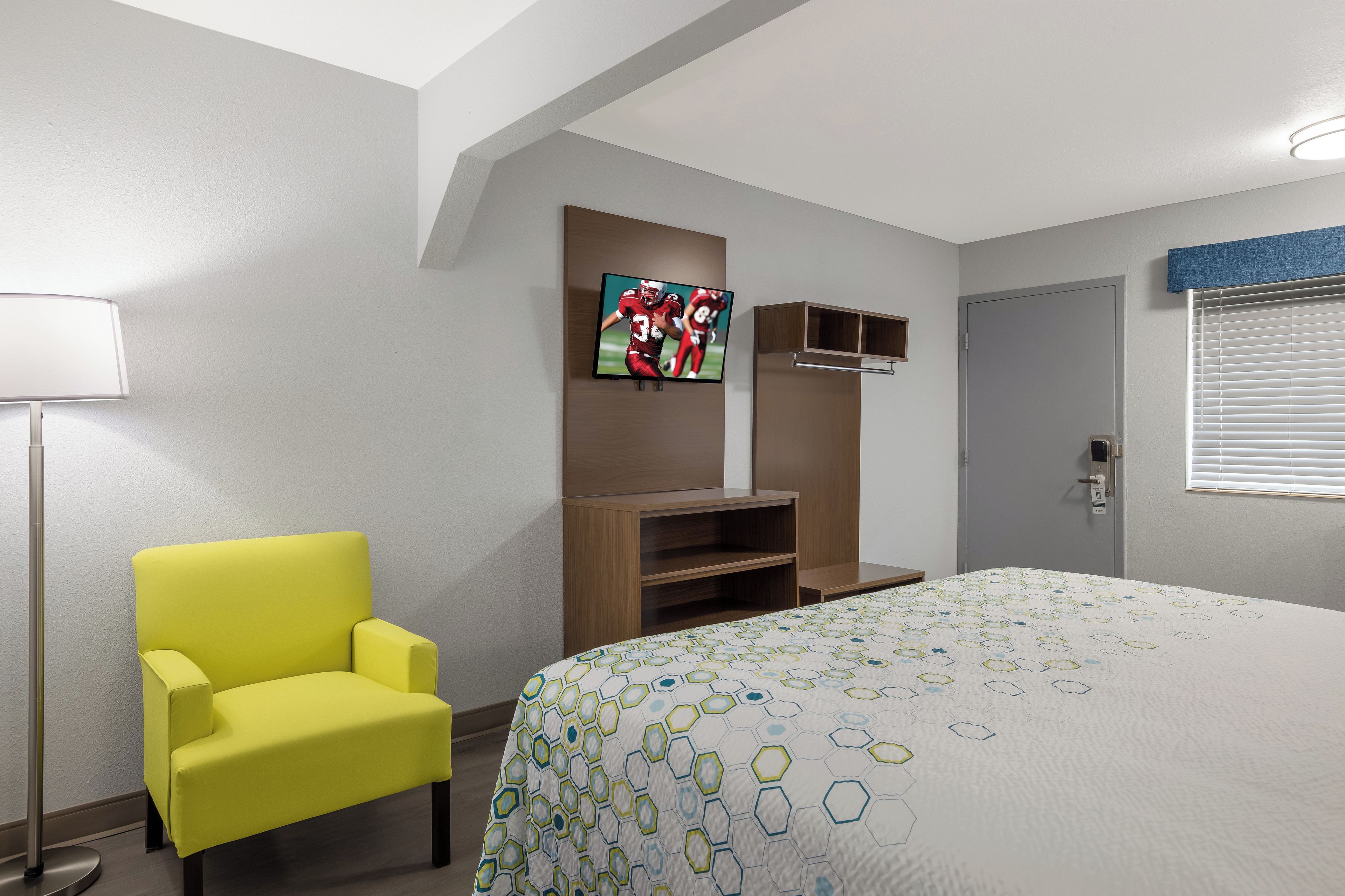 Habitació d'hotel amb un llit, un butaca groga, una televisió i un armari.