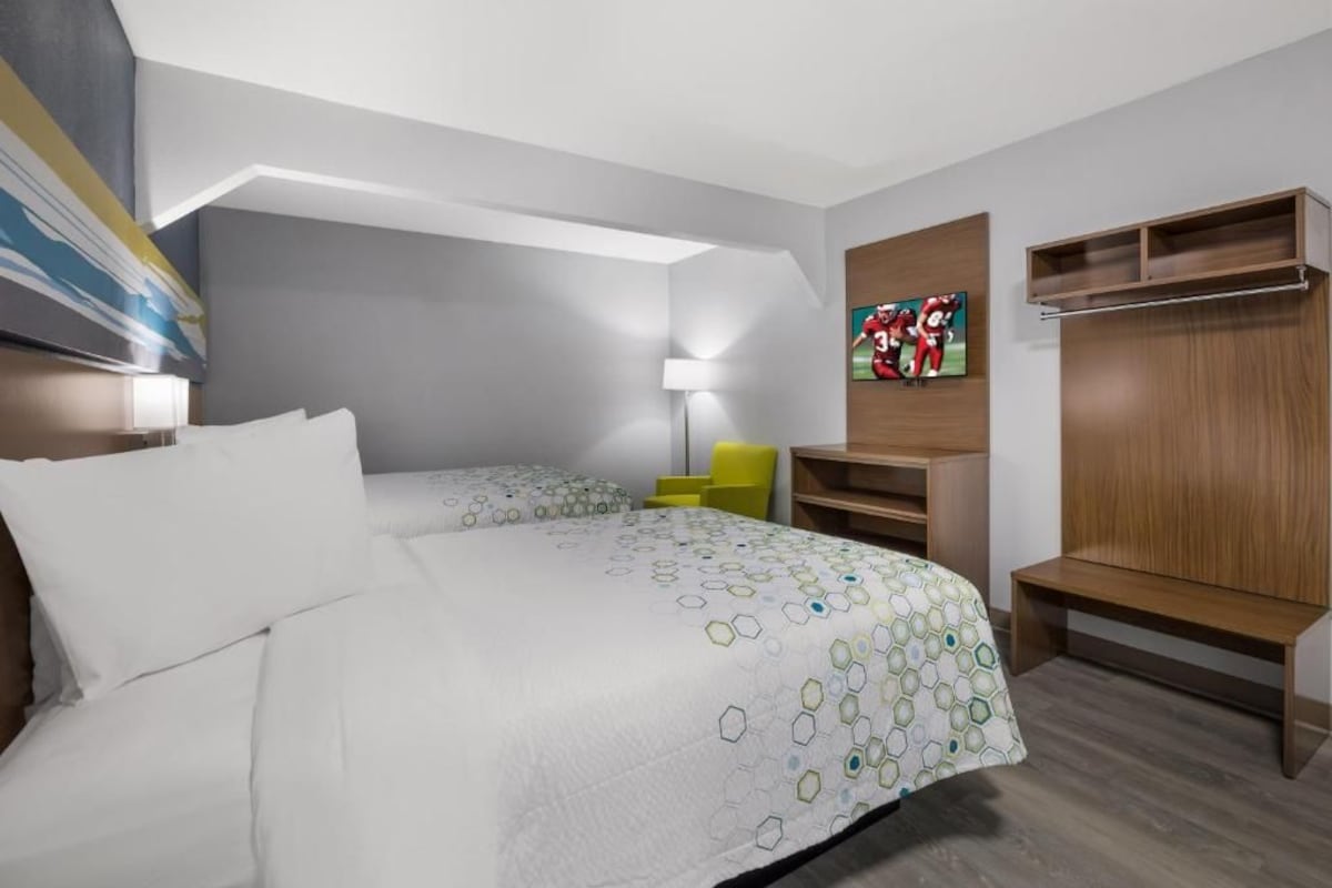 A hotel room with a bed, a desk, a chair, a lamp, and a wardrobe.
