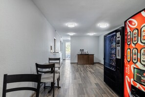 A modern interior with a vending machine, a wooden cabinet, and a seating area with chairs and a table. - HomeTowne Studios by Red Roof Orange, TX (Orange)
