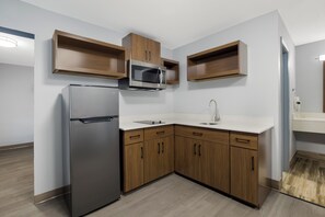 A modern kitchen with a built-in microwave, refrigerator, and wooden cabinets. - HomeTowne Studios by Red Roof Orange, TX (Orange)