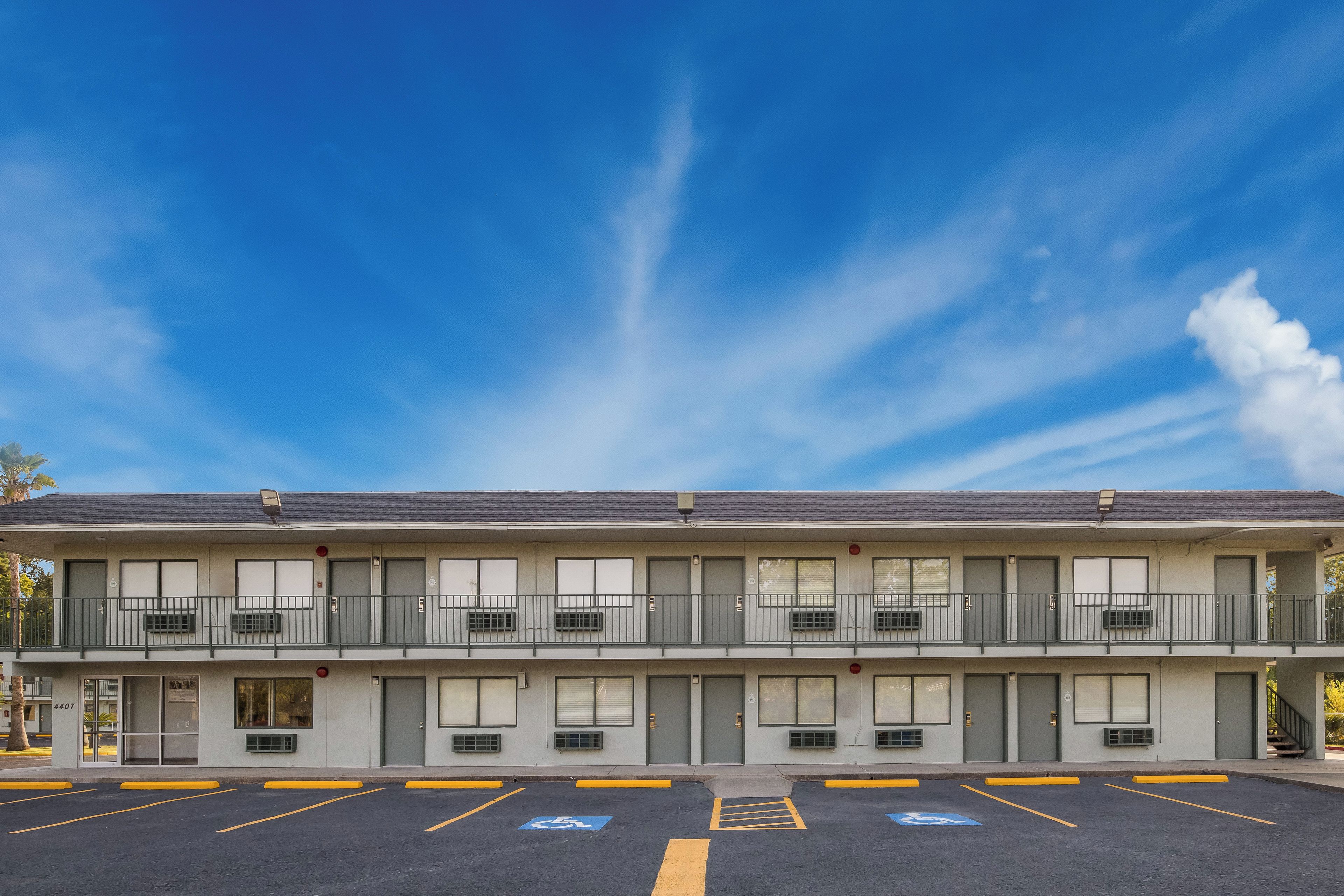 A two-story motel with a parking lot, marked handicap spaces, and a clear blue sky.