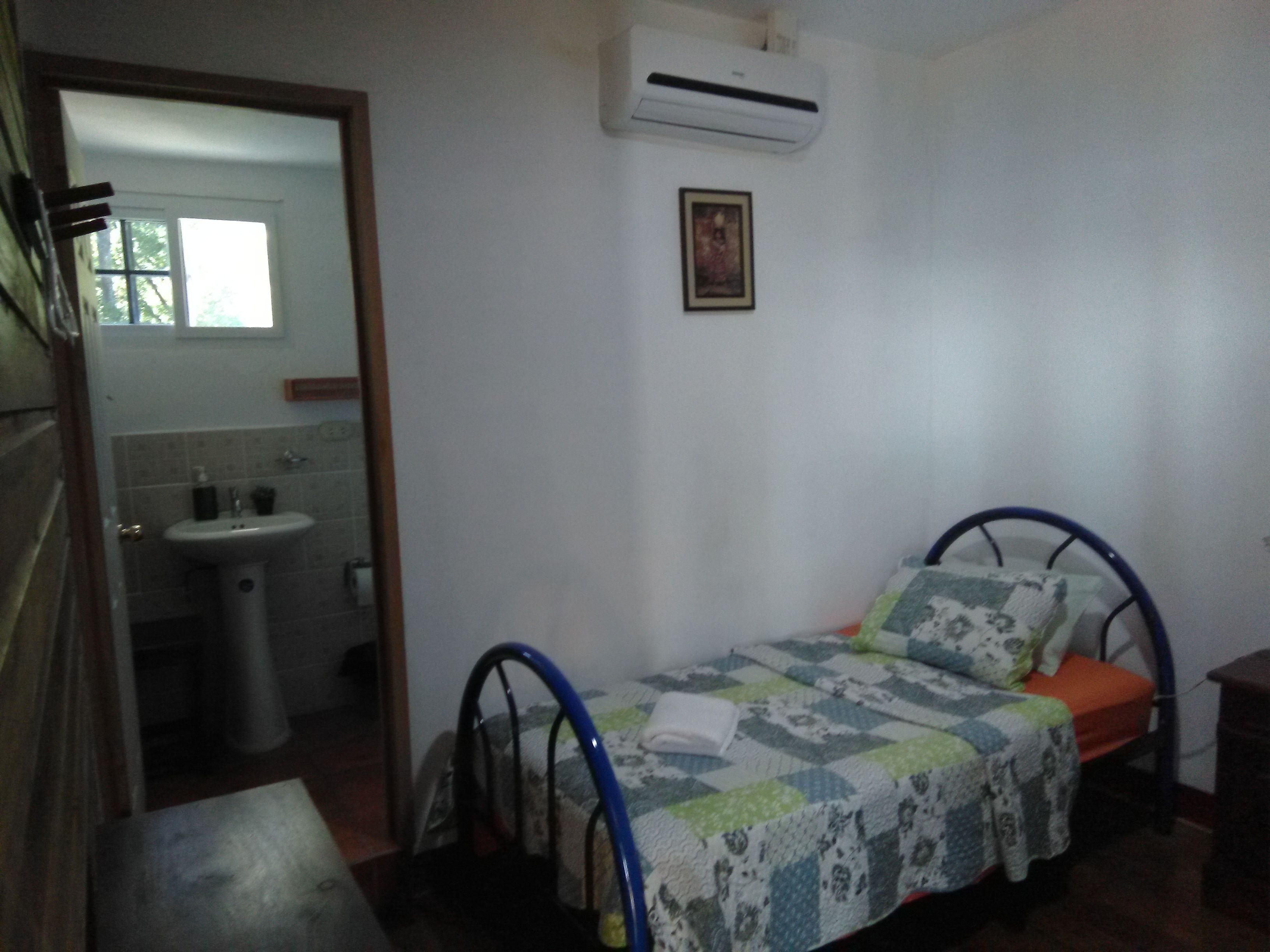 A small, simple room with a bed, a sink, and an air conditioning unit.