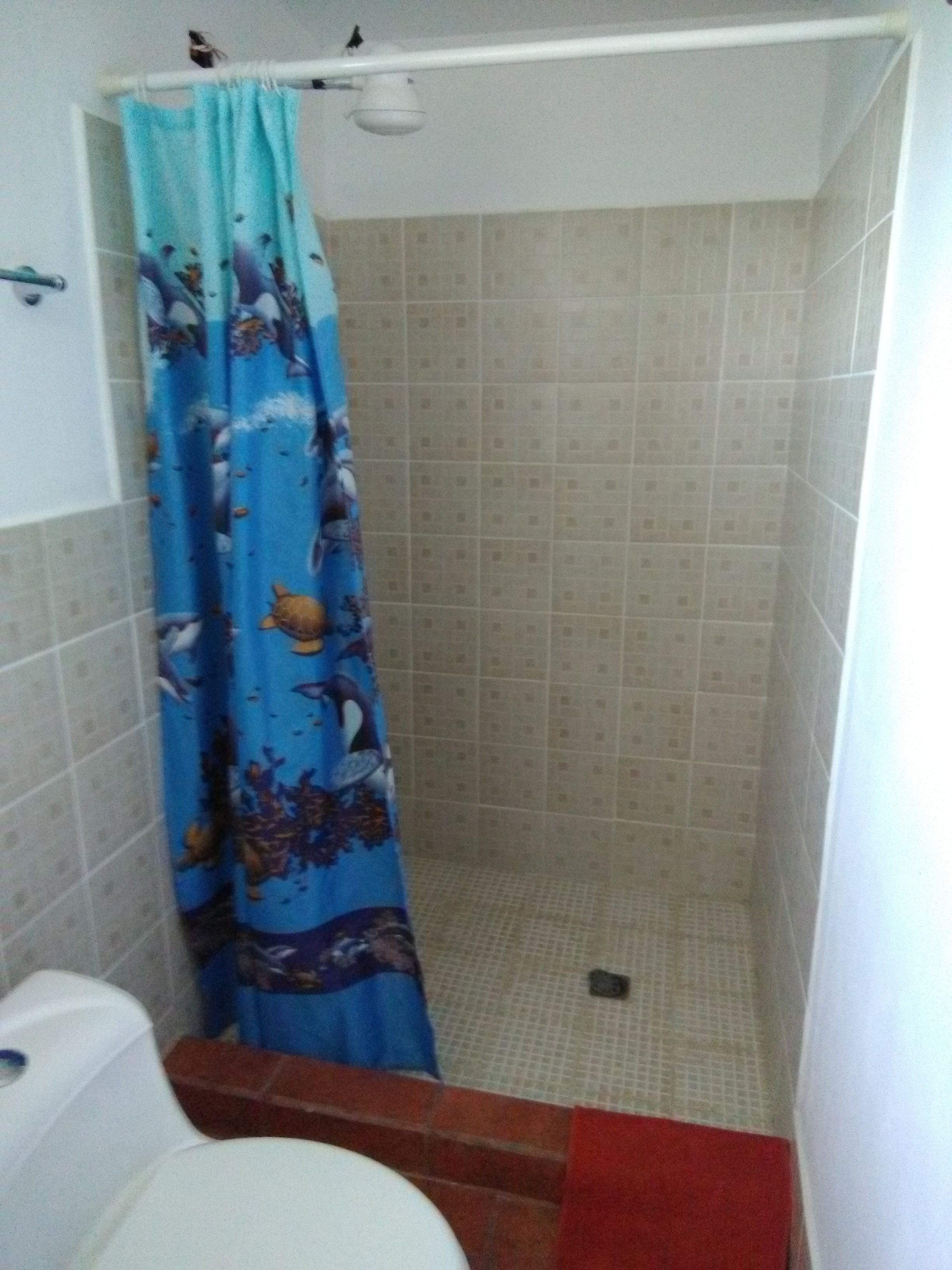 Un baño pequeño con cortina de ducha, un inodoro y una toalla roja en el suelo.