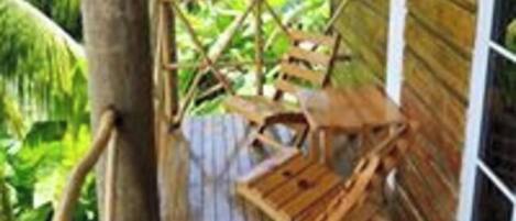 A wooden deck with a wooden chair and a table, surrounded by lush greenery.