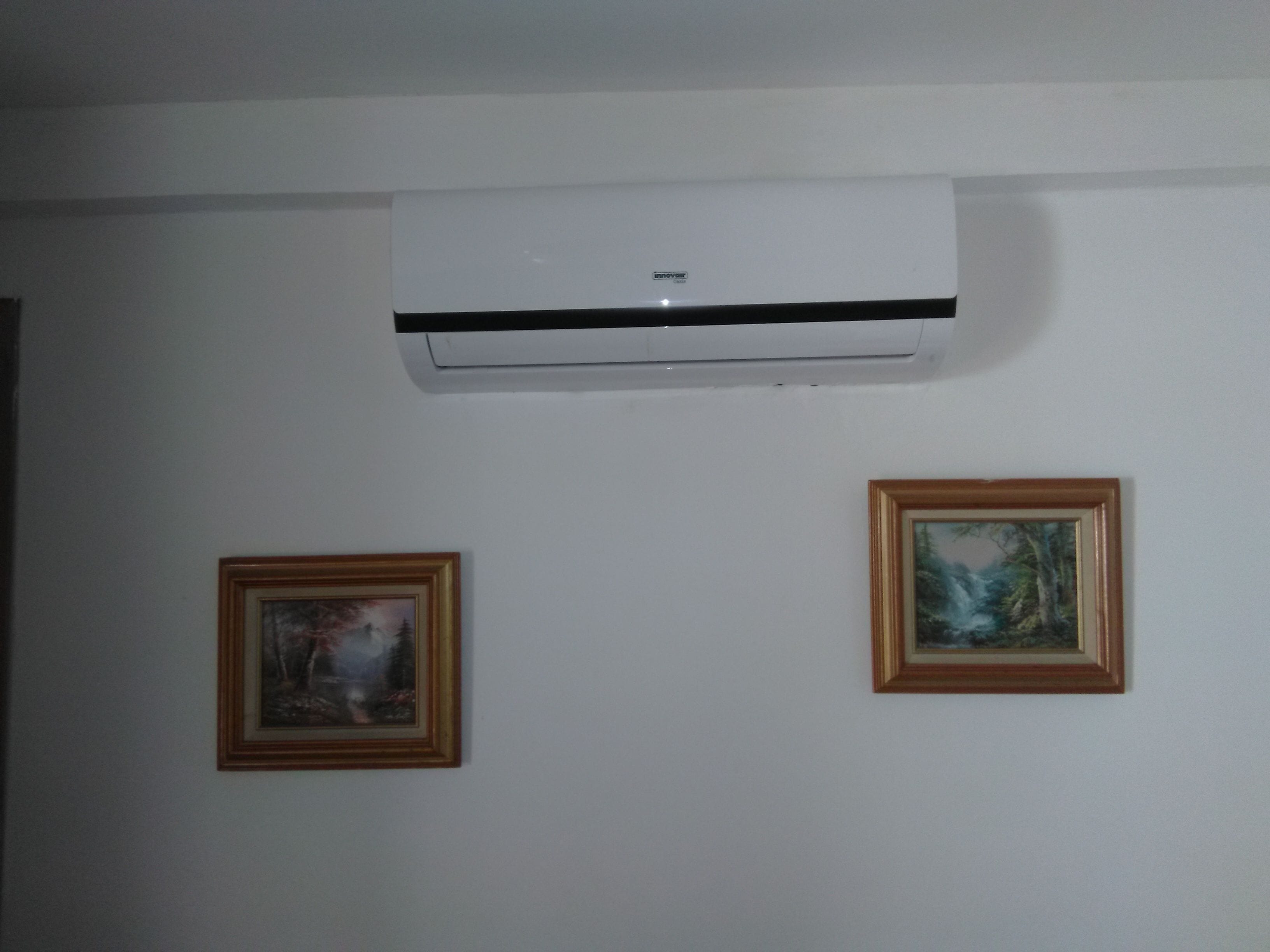 Una habitación con un equipo de aire acondicionado en la pared, dos cuadros enmarcados y un techo blanco.