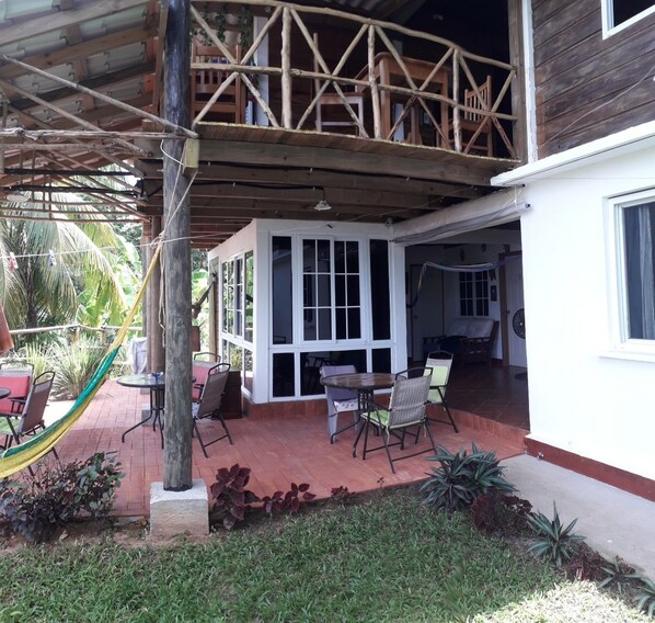 Un patio techado con mobiliario exterior, una hamaca y vista al interior.