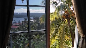 Una ventana con vista a un paisaje tropical, incluyendo palmeras y una masa de agua.