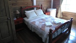 Un dormitorio con paneles de madera, una cama, mesitas de noche, una lámpara y un ventanal con cortinas.