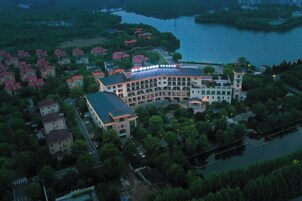 A large, multi-story building with a curved facade, surrounded by trees and a body of water.