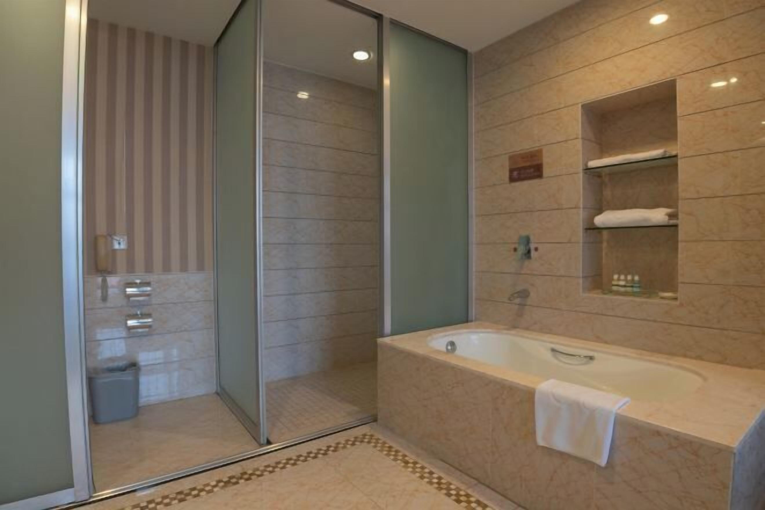A modern bathroom with a glass shower enclosure, a freestanding bathtub, and a marble-tiled wall.