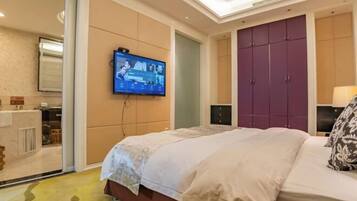 A hotel room with a bed, a television mounted on the wall, a wardrobe, and a small table with a lamp.