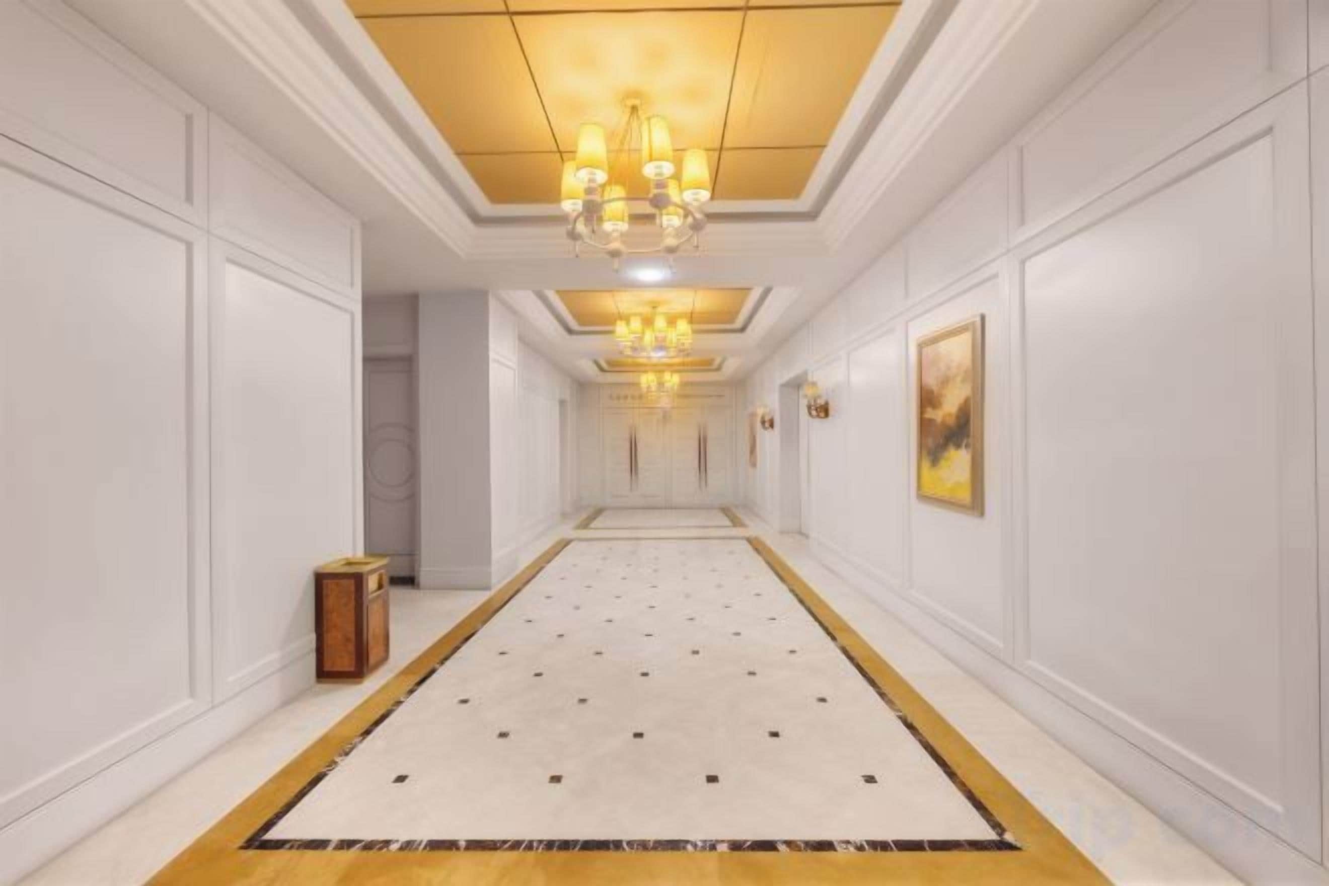 A corridor with a patterned carpet, white walls, and a chandelier.