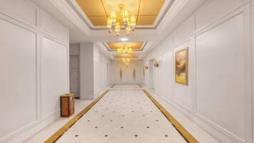 A corridor with a patterned carpet, white walls, and a chandelier.