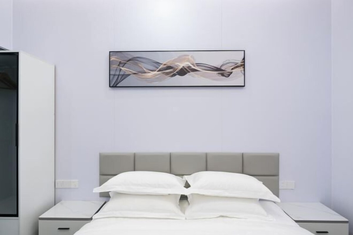 A modern bedroom with a bed, nightstands, and a wall-mounted abstract artwork.